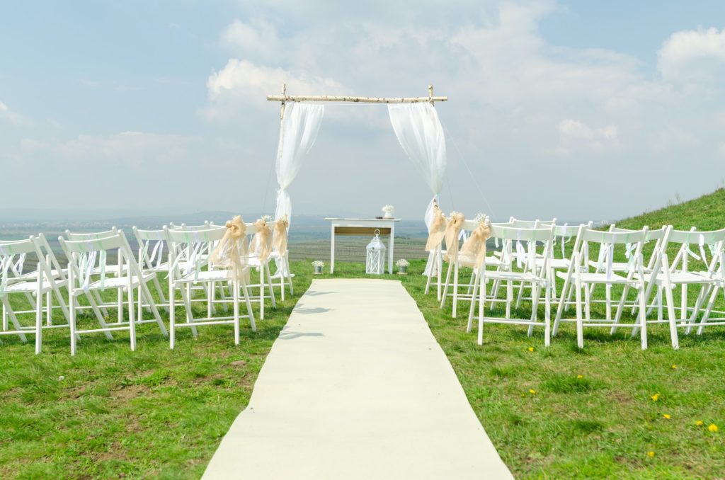 Outdoor wedding ceremony with empty white chairs and an altar adorned with a birdcage and white table.